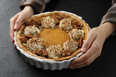 Woman with homemade pumpkin pie with whipped cream, seeds and cinnamon at black table, closeup