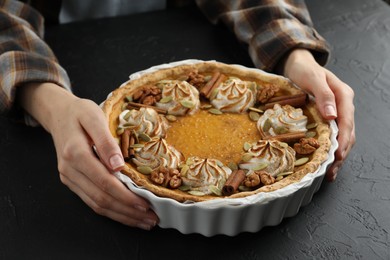 Woman with homemade pumpkin pie with whipped cream, seeds and cinnamon at black table, closeup