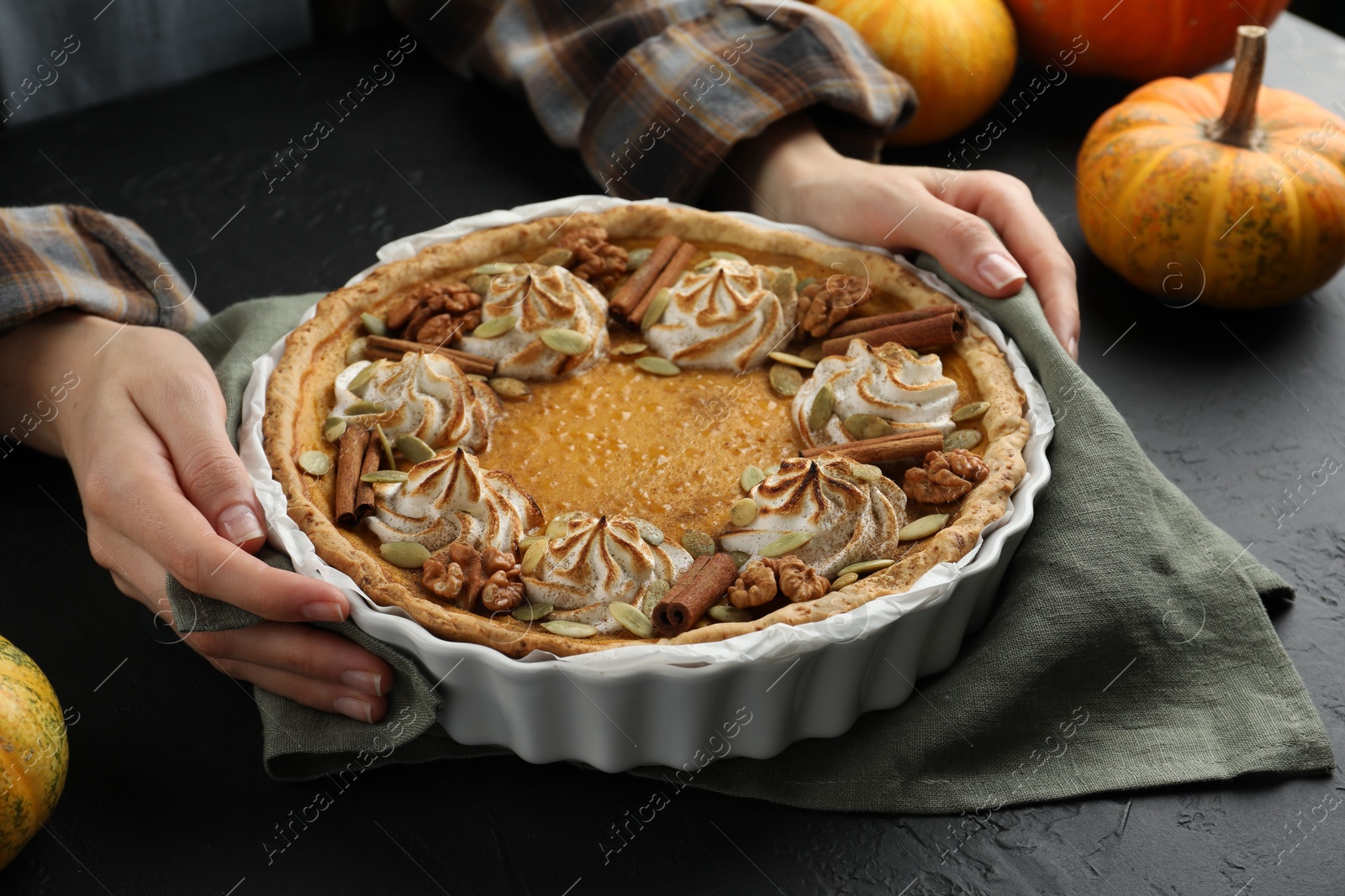 Photo of Woman with homemade pumpkin pie with whipped cream, seeds and cinnamon at black table, closeup