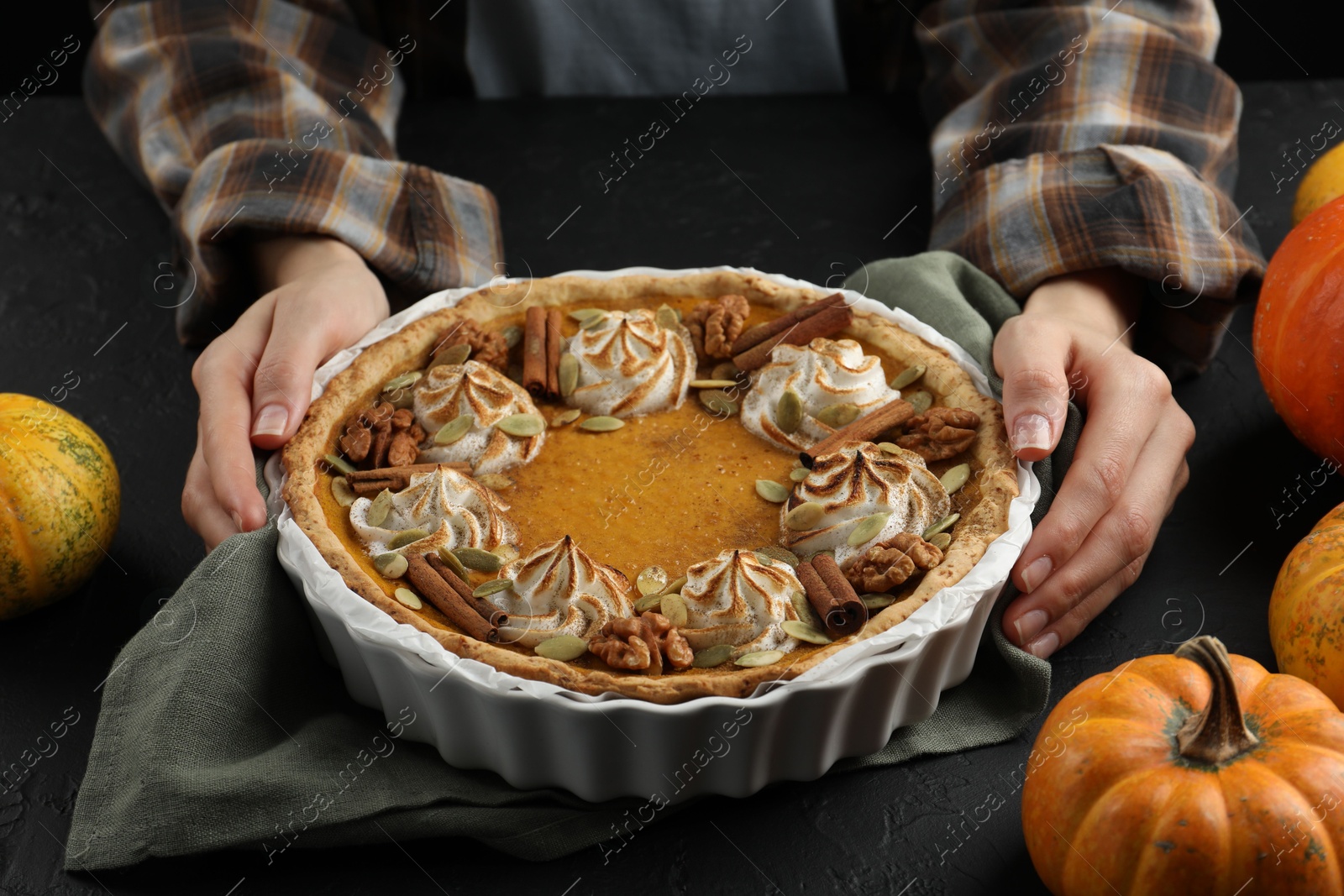 Photo of Woman with homemade pumpkin pie with whipped cream, seeds and cinnamon at black table, closeup