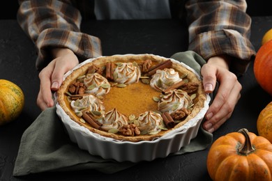 Photo of Woman with homemade pumpkin pie with whipped cream, seeds and cinnamon at black table, closeup