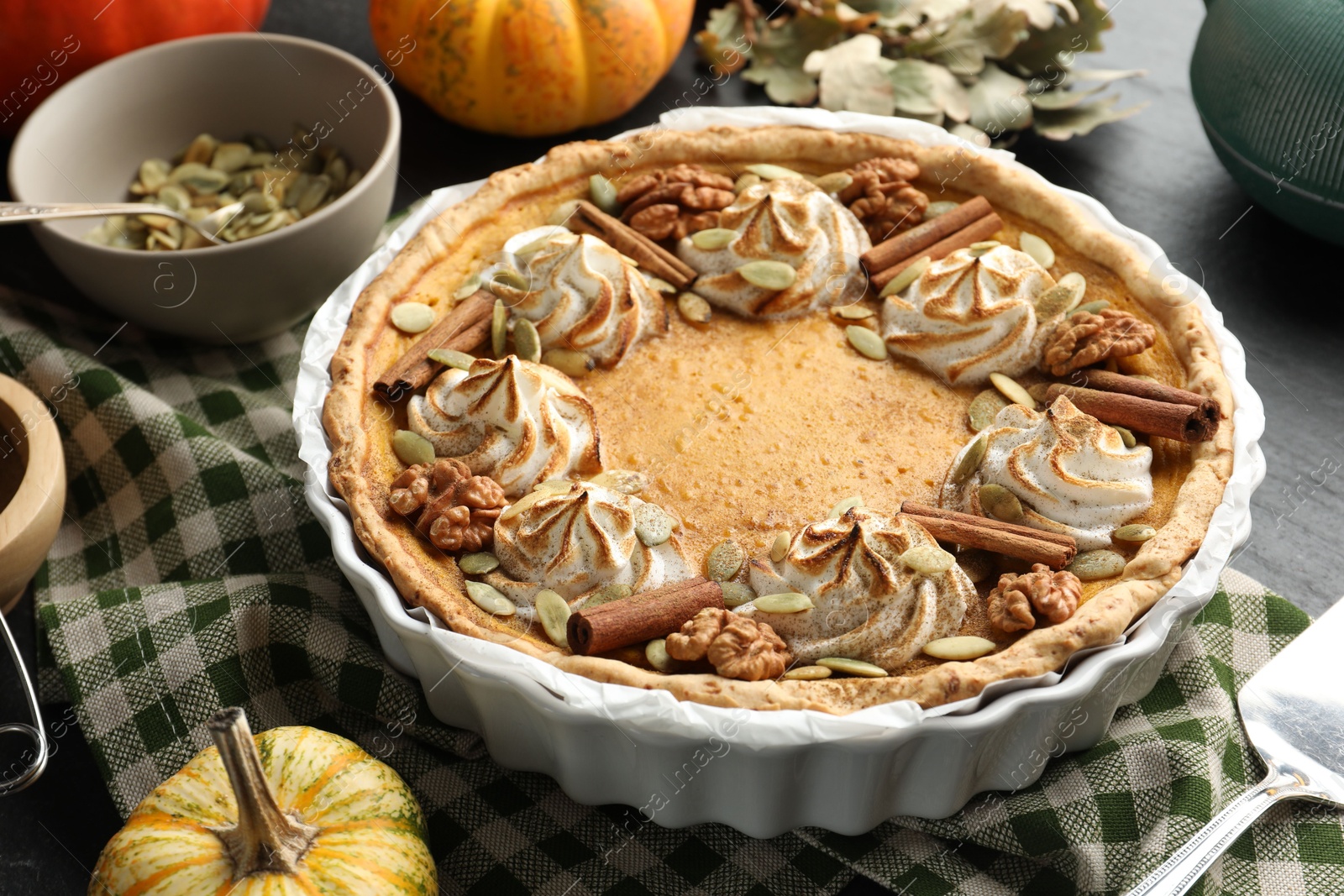 Photo of Homemade pumpkin pie with whipped cream, seeds and cinnamon on grey table, closeup