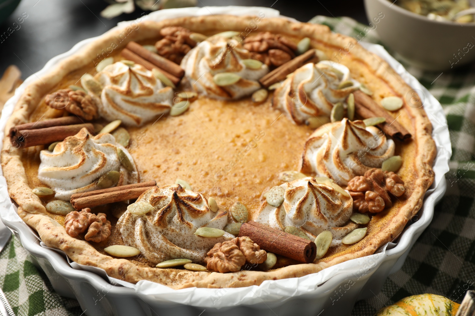 Photo of Homemade pumpkin pie with whipped cream, seeds and cinnamon on table, closeup