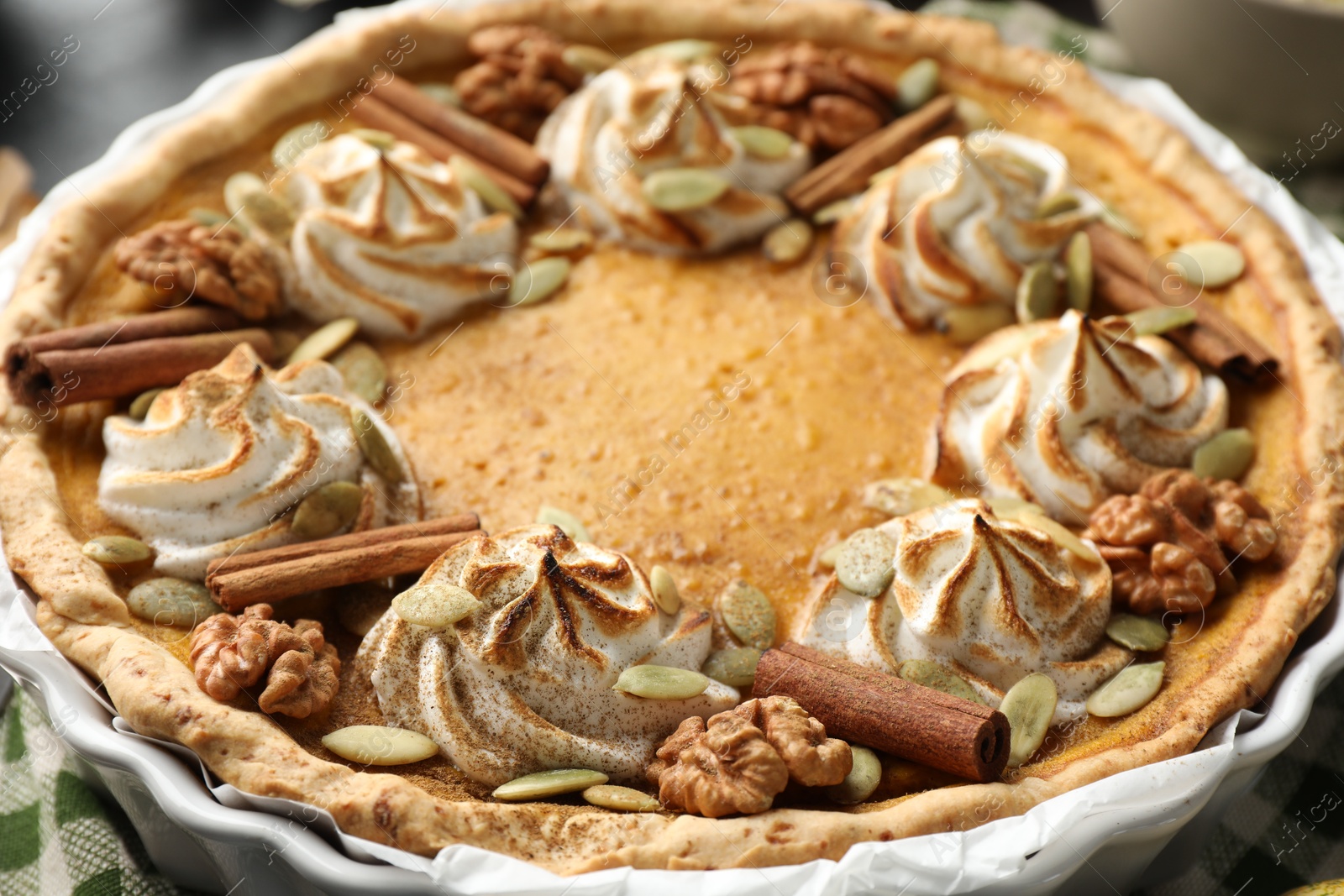 Photo of Homemade pumpkin pie with whipped cream, seeds and cinnamon on table, closeup