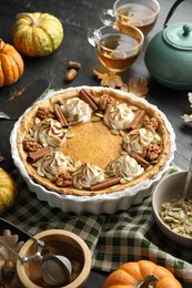 Homemade pumpkin pie with whipped cream, seeds and cinnamon on grey table