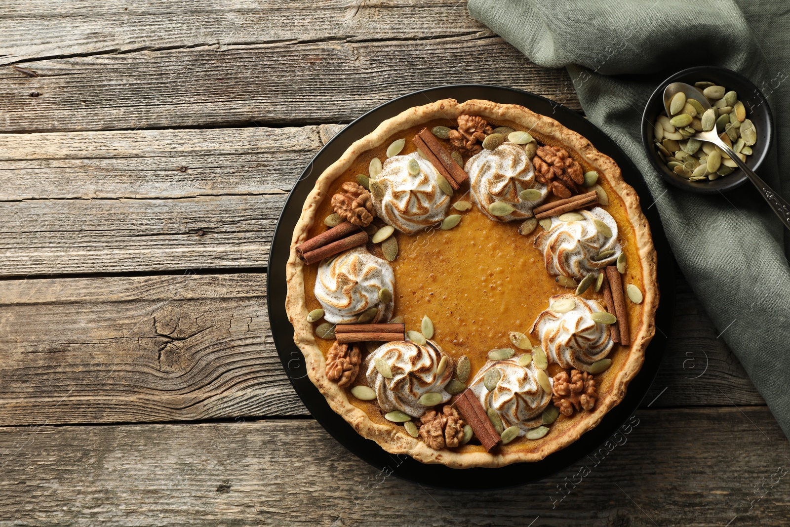 Photo of Homemade pumpkin pie with whipped cream, seeds and cinnamon on wooden table, top view. Space for text