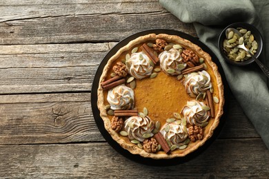 Homemade pumpkin pie with whipped cream, seeds and cinnamon on wooden table, top view. Space for text