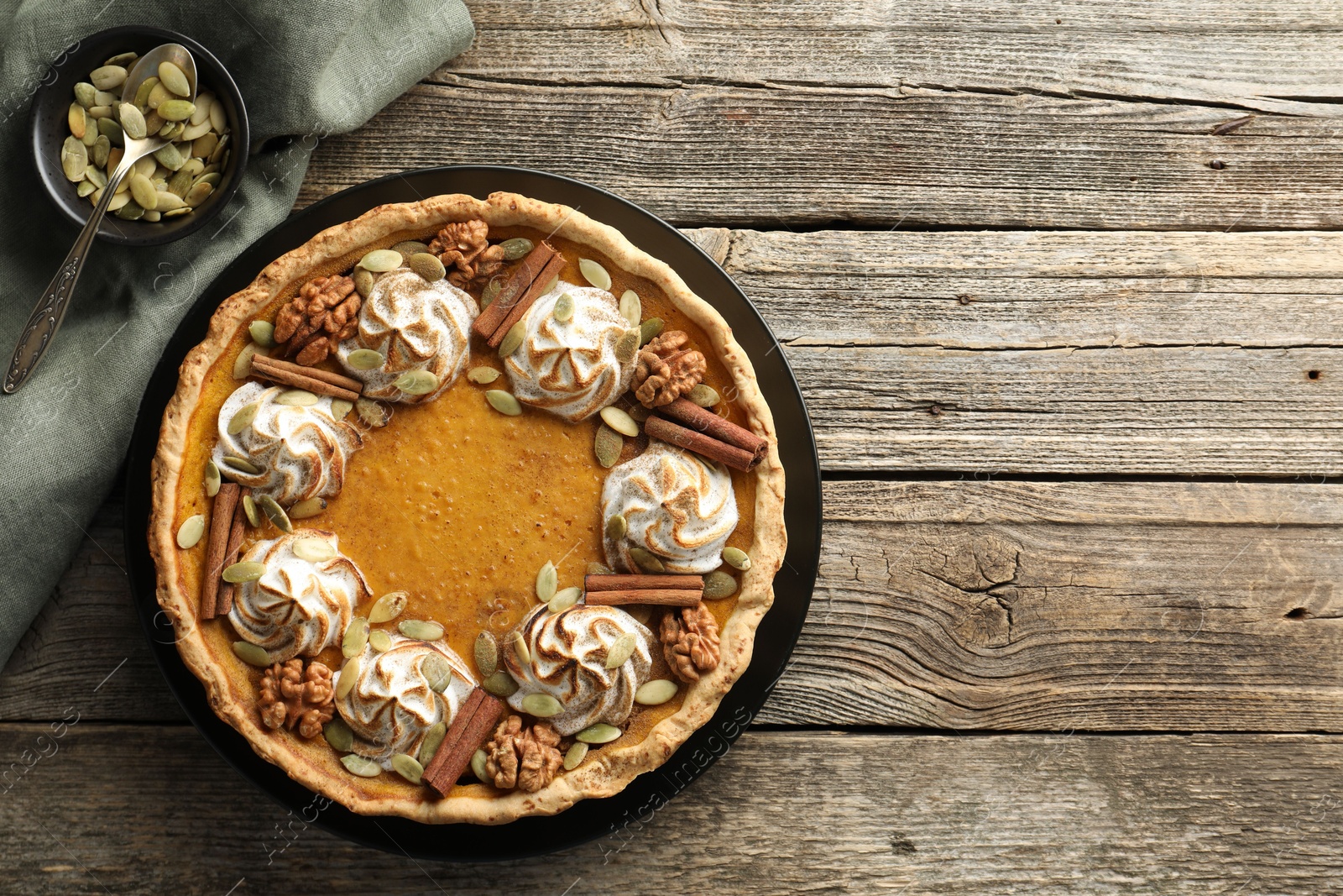 Photo of Homemade pumpkin pie with whipped cream, seeds and cinnamon on wooden table, top view. Space for text