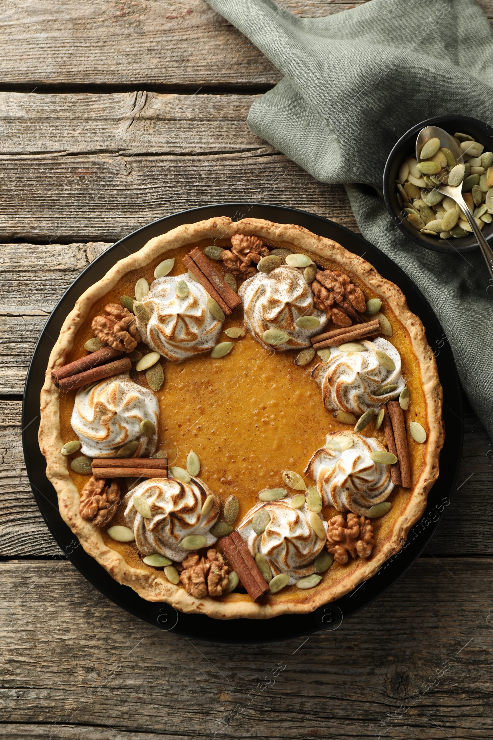 Photo of Homemade pumpkin pie with whipped cream, seeds and cinnamon on wooden table, top view