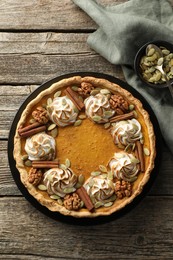 Photo of Homemade pumpkin pie with whipped cream, seeds and cinnamon on wooden table, top view