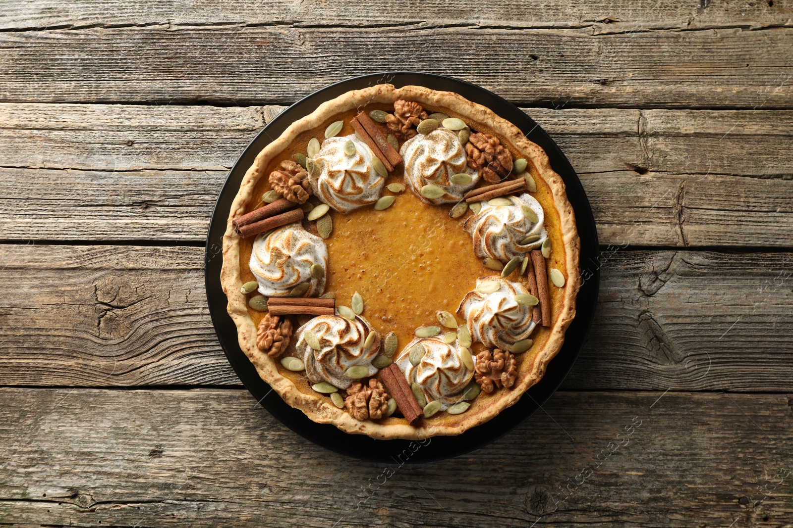 Photo of Homemade pumpkin pie with whipped cream, seeds and cinnamon on wooden table, top view