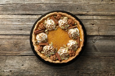 Homemade pumpkin pie with whipped cream, seeds and cinnamon on wooden table, top view