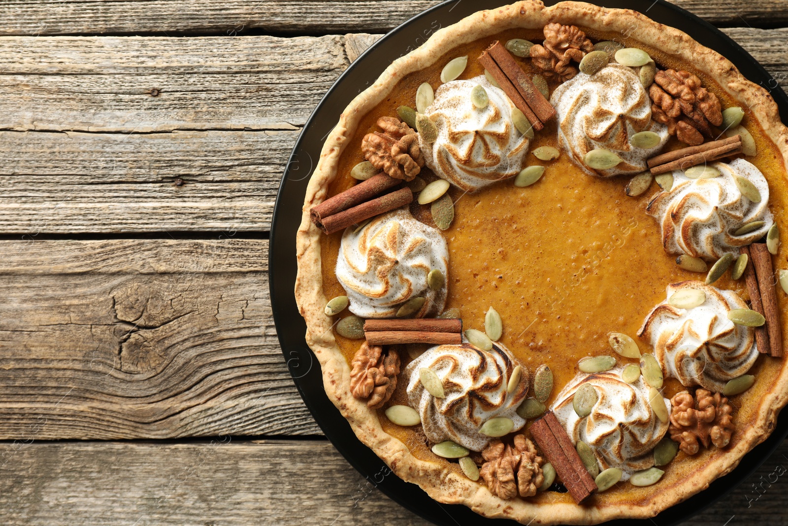 Photo of Homemade pumpkin pie with whipped cream, seeds and cinnamon on wooden table, top view. Space for text