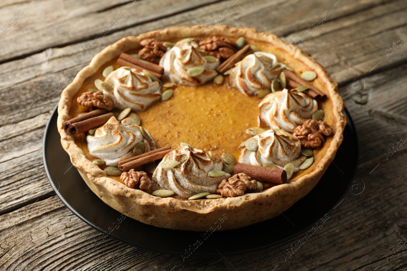 Photo of Homemade pumpkin pie with whipped cream, seeds and cinnamon on wooden table