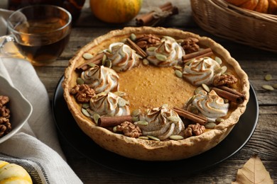 Photo of Homemade pumpkin pie with whipped cream, seeds and cinnamon on wooden table