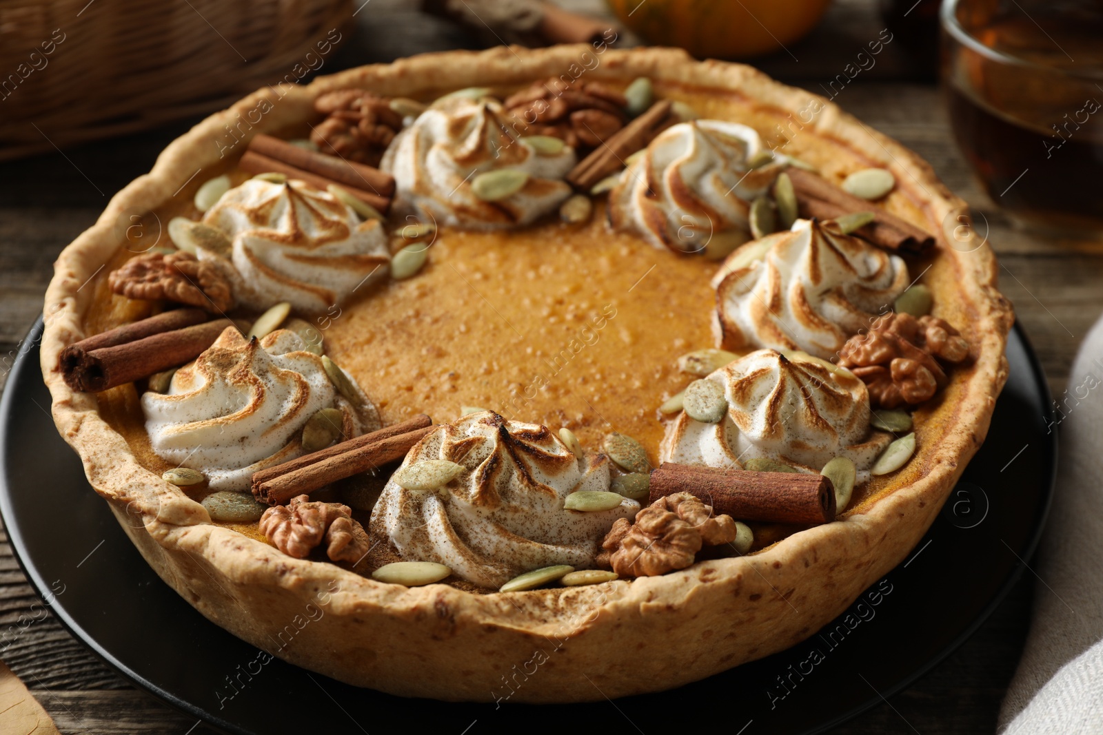 Photo of Homemade pumpkin pie with whipped cream, seeds and cinnamon on wooden table, closeup