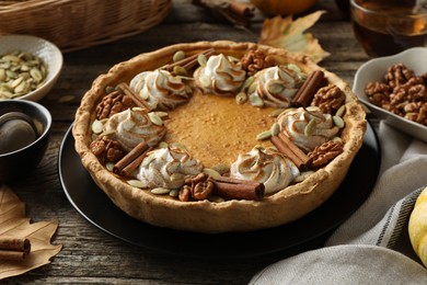 Homemade pumpkin pie with whipped cream, seeds and cinnamon on wooden table