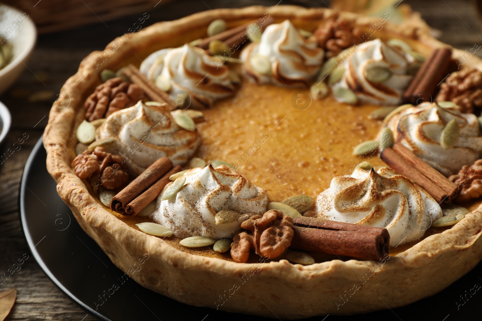 Photo of Homemade pumpkin pie with whipped cream, seeds and cinnamon on wooden table, closeup