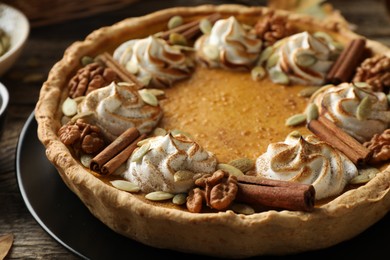 Photo of Homemade pumpkin pie with whipped cream, seeds and cinnamon on wooden table, closeup