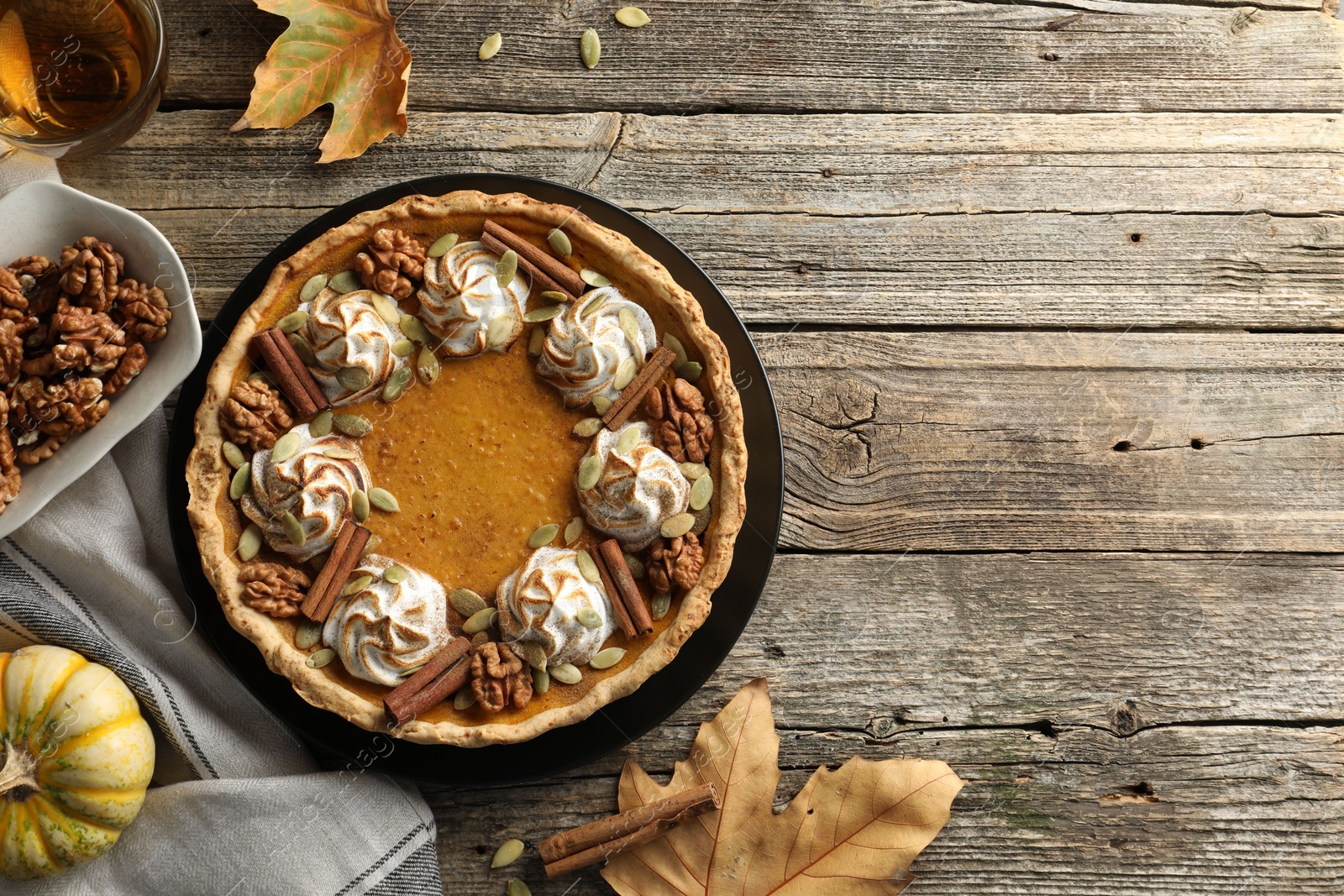 Photo of Flat lay composition with homemade pumpkin pie with whipped cream, seeds and cinnamon on wooden table, space for text