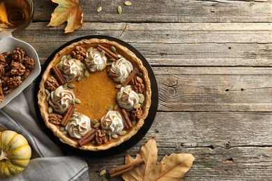 Photo of Flat lay composition with homemade pumpkin pie with whipped cream, seeds and cinnamon on wooden table, space for text