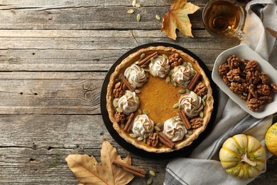 Flat lay composition with homemade pumpkin pie with whipped cream, seeds and cinnamon on wooden table, space for text