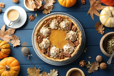 Flat lay composition with homemade pumpkin pie with whipped cream, seeds and cinnamon on blue wooden table