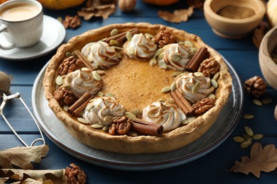 Photo of Homemade pumpkin pie with whipped cream, seeds and cinnamon on blue wooden table