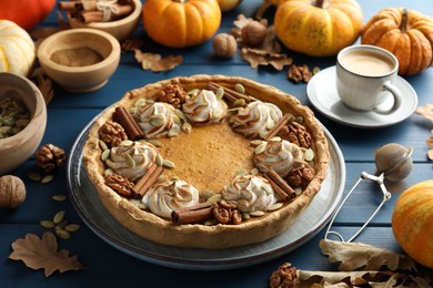 Photo of Homemade pumpkin pie with whipped cream, seeds and cinnamon on blue wooden table