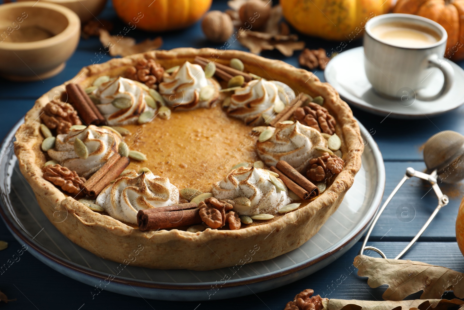 Photo of Homemade pumpkin pie with whipped cream, seeds and cinnamon on blue wooden table, closeup