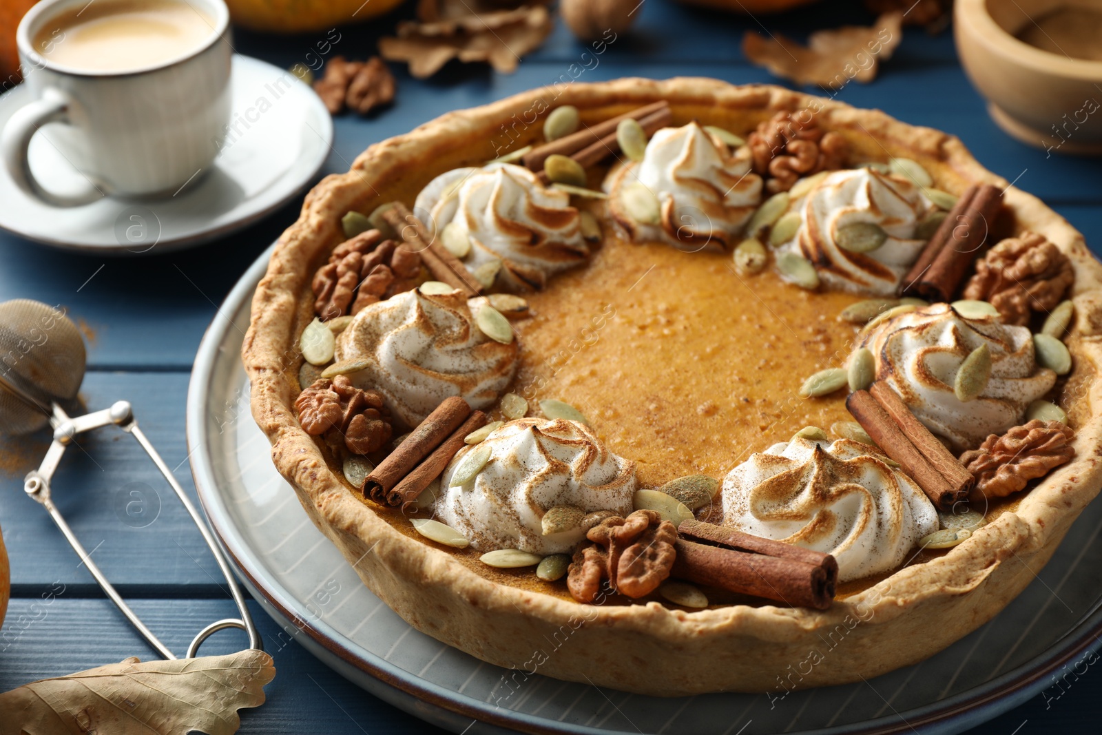 Photo of Homemade pumpkin pie with whipped cream, seeds and cinnamon on blue wooden table, closeup