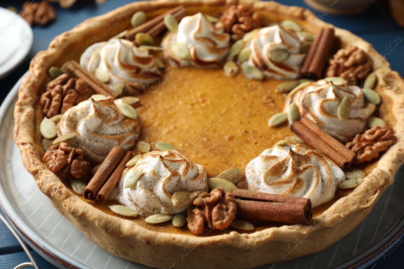 Photo of Homemade pumpkin pie with whipped cream, seeds and cinnamon on blue wooden table, closeup