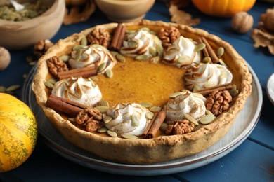 Homemade pumpkin pie with whipped cream, seeds and cinnamon on blue wooden table, closeup