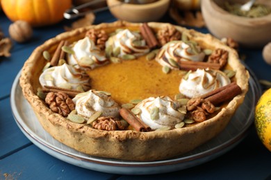 Homemade pumpkin pie with whipped cream, seeds and cinnamon on blue wooden table, closeup