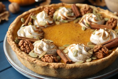 Photo of Homemade pumpkin pie with whipped cream, seeds and cinnamon on blue wooden table, closeup