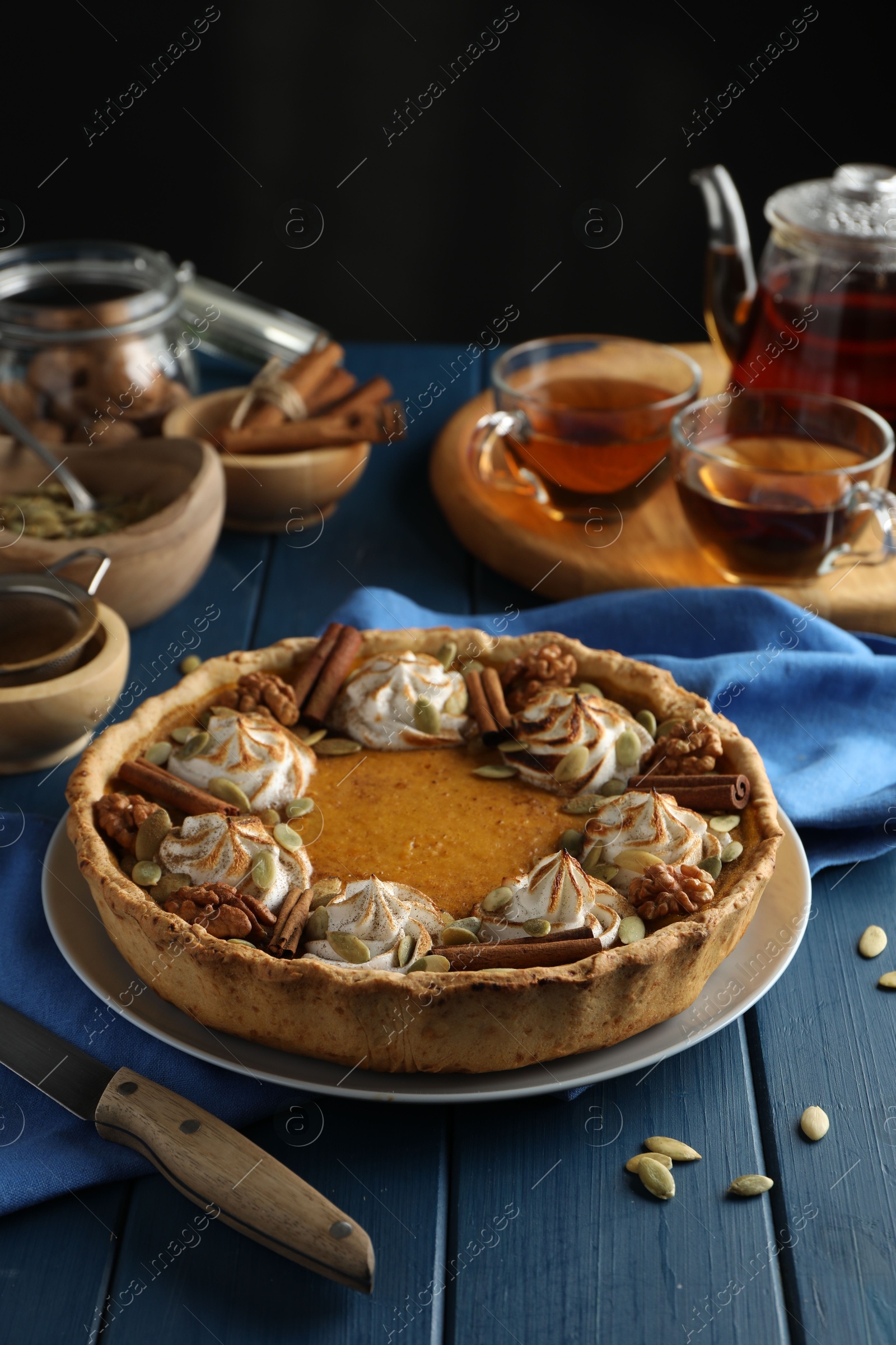 Photo of Homemade pumpkin pie with whipped cream, seeds and cinnamon on blue wooden table