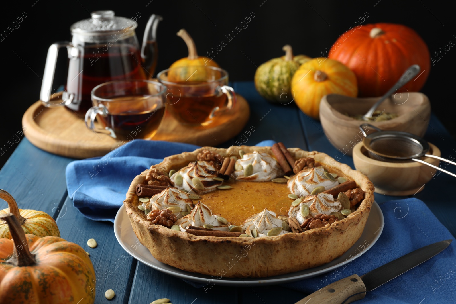 Photo of Homemade pumpkin pie with whipped cream, seeds and cinnamon on blue wooden table