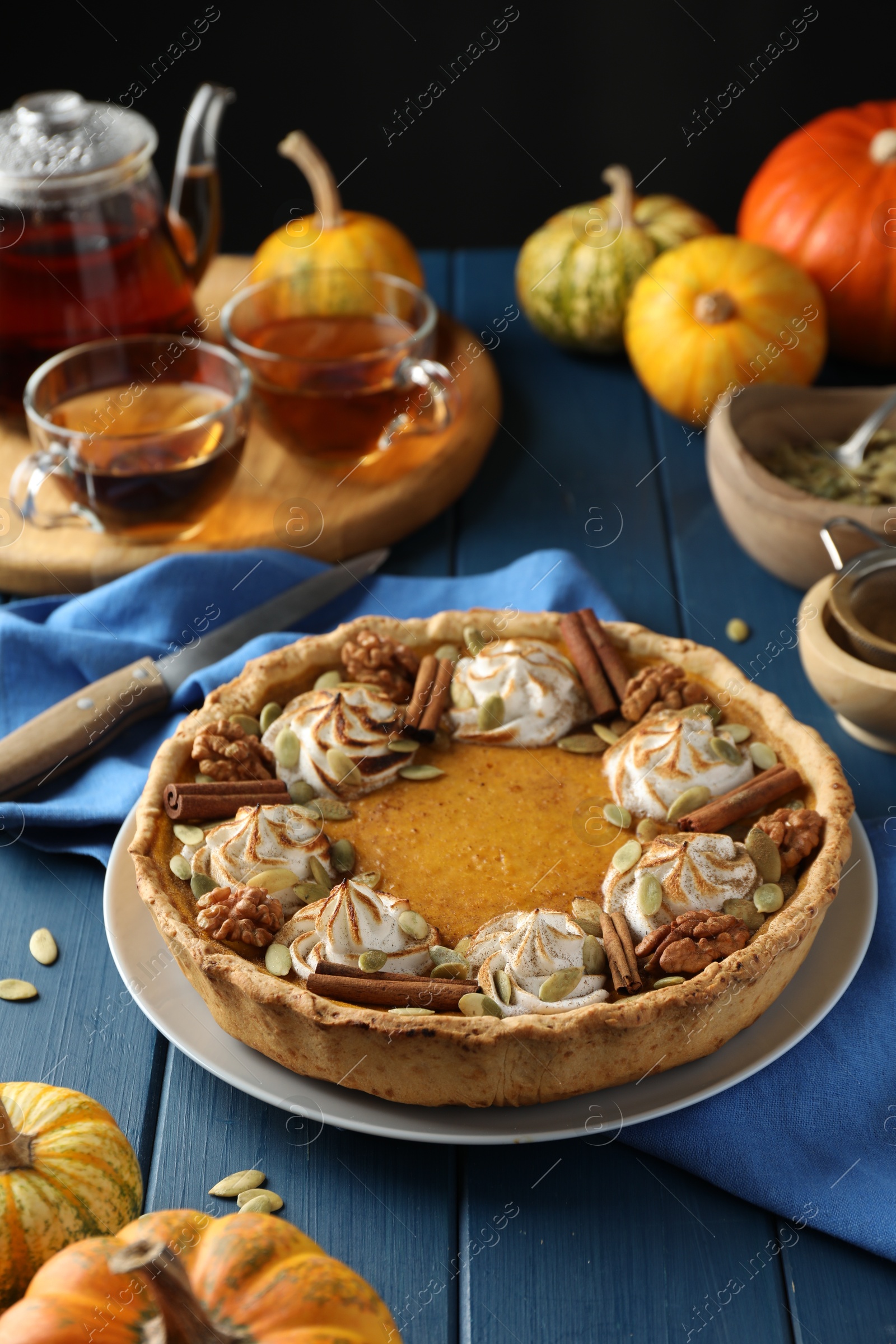 Photo of Homemade pumpkin pie with whipped cream, seeds and cinnamon on blue wooden table