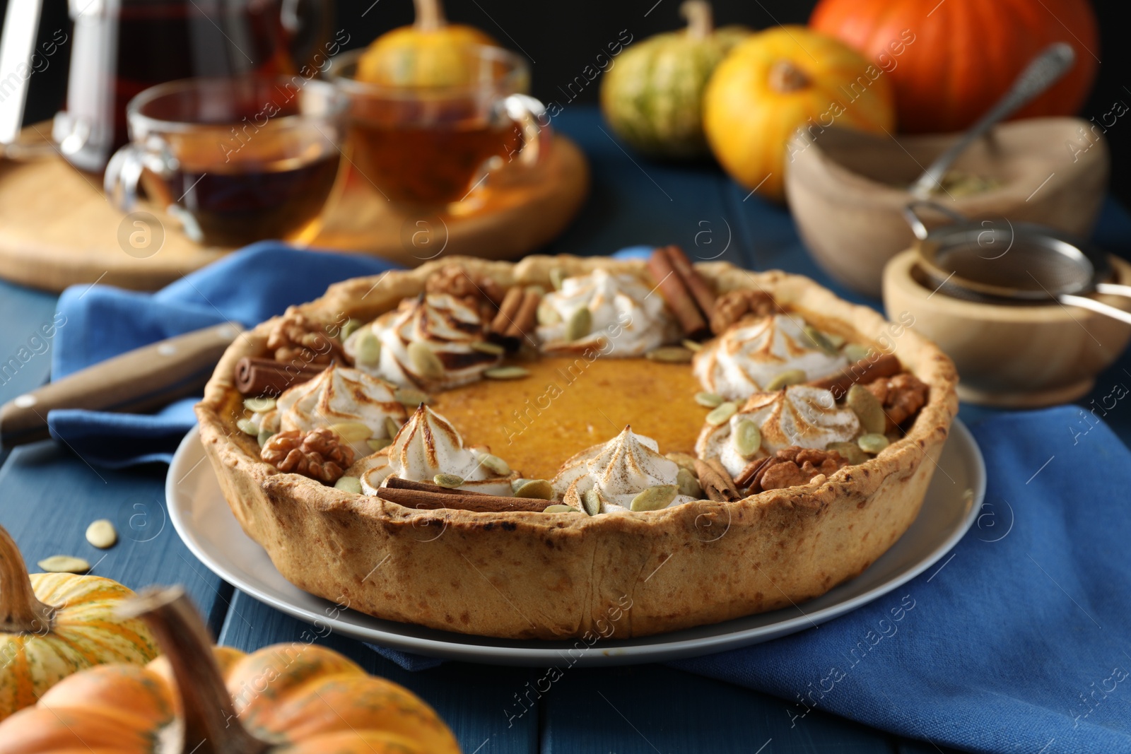 Photo of Homemade pumpkin pie with whipped cream, seeds and cinnamon on blue wooden table