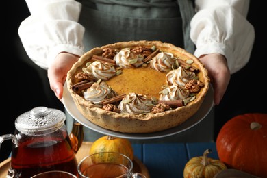 Woman with homemade pumpkin pie with whipped cream, seeds and cinnamon at blue wooden table, closeup