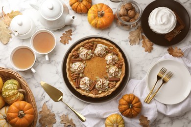 Flat lay composition with homemade pumpkin pie with whipped cream, seeds and cinnamon on white marble table