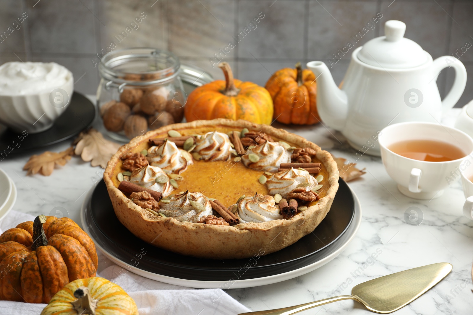 Photo of Homemade pumpkin pie with whipped cream, seeds and cinnamon on white marble table