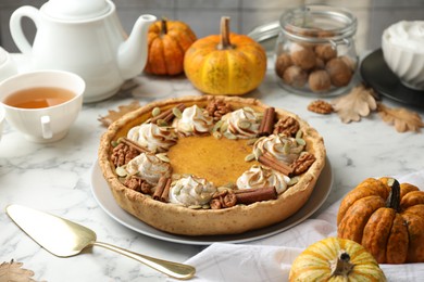 Photo of Homemade pumpkin pie with whipped cream, seeds and cinnamon on white marble table