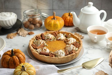 Photo of Homemade pumpkin pie with whipped cream, seeds and cinnamon on white marble table