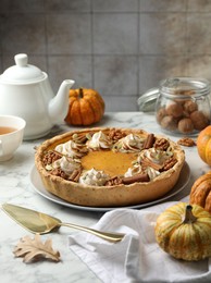 Homemade pumpkin pie with whipped cream, seeds and cinnamon on white marble table