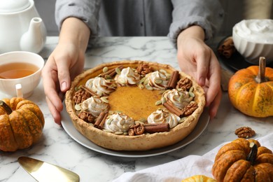 Photo of Woman with homemade pumpkin pie with whipped cream, seeds and cinnamon at white marble table, closeup