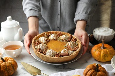 Woman with homemade pumpkin pie with whipped cream, seeds and cinnamon at white marble table, closeup