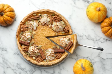 Photo of Tasty homemade pumpkin pie with ingredients and server on white marble table, flat lay