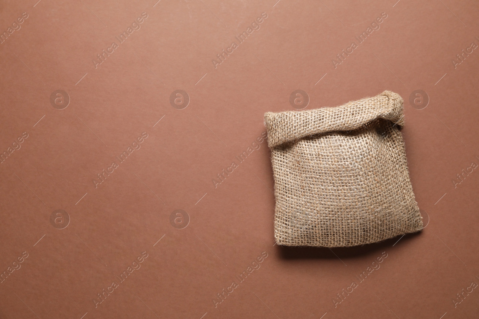 Photo of One burlap sack on brown background, top view. Space for text