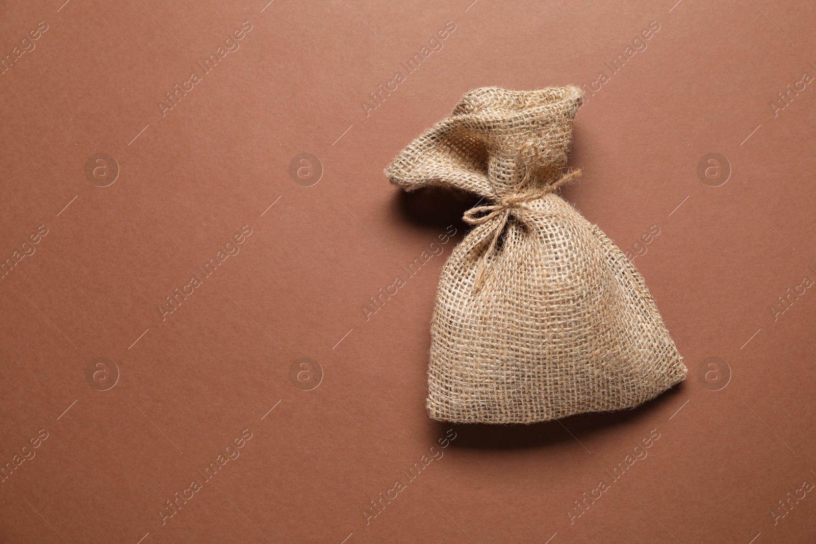 Photo of One burlap sack on brown background, top view. Space for text